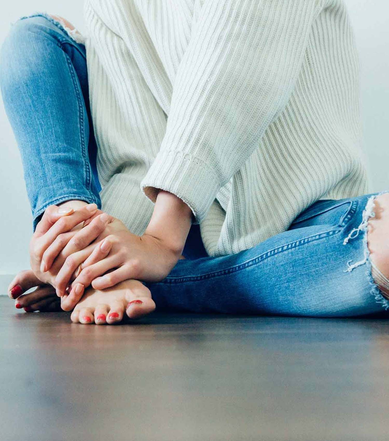 Teenage girl with period cramps clasping hands sitting on floor